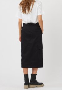 Hame skirt hitam terbuat dari katun, panjang di lutut dengan saku samping dan pinggang ketat. Dipadukan dengan sepatu bot pergelangan kaki hitam dan kaus putih.