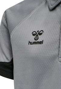 Grå atletisk polo tröja med ett strukturerat mönster, med svarta detaljer och en svart "hummel"-logotyp på vänster bröstområde.
