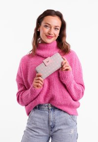 Gray wallet with light pink floral pattern, clasp closure, and logo accent, held by a person wearing a pink knit sweater.