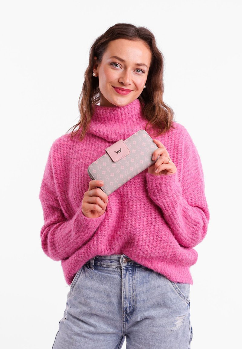 Gray wallet with light pink floral pattern, clasp closure, and logo accent, held by a person wearing a pink knit sweater.