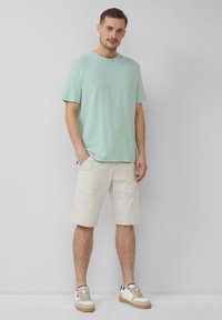 Miętowa koszulka z krótkim rękawem w połączeniu ze światłobeżowymi szortami do kolan. Sneakersy z białymi i beżowymi akcentami. Prosty, casualowy wygląd.