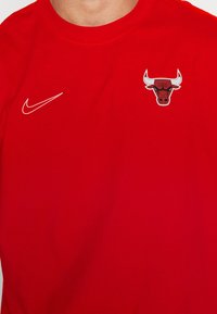 Camisa roja con el logo de Nike en blanco en el lado izquierdo del pecho y el logo de los Chicago Bulls en el lado derecho del pecho, llevada por una persona.