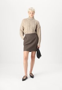Jersey beige de punto con cuello alto, combinado con una falda ajustada de cuadros marrones. Un bolso negro y zapatos planos de punta completan el look.