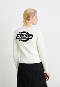 White sweater with a black "Dickies" logo on the back, featuring a fitted design, ribbed cuffs, and a soft, textured material.