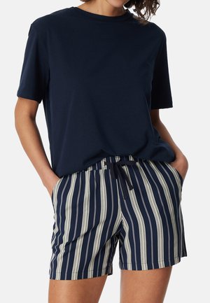 Persona che indossa una maglietta a maniche corte blu navy e pantaloncini blu navy con strisce verticali bianche e vita con coulisse.
