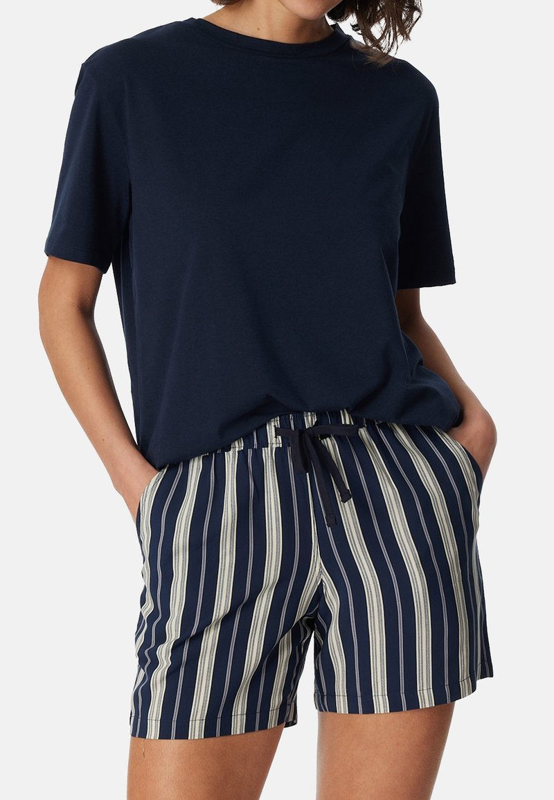 Personne portant un t-shirt à manches courtes bleu marine et un short bleu marine avec des rayures verticales blanches et une taille à cordon.