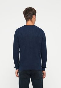 Pull en maille bleu marine avec un motif en côtes texturé, col rond et manches longues, associé à un jean foncé.