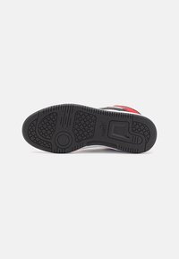 Semelle de chaussure en caoutchouc noir avec motifs de grip texturés, dotée d'un bout arrondi et d'un marquage minimal. Accents de couleur rouge et blanc.