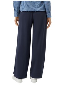 Donkere marineblauwe wijde broek van zachte stof, met een gladde textuur en elastische tailleband, gecombineerd met witte platte sneakers.