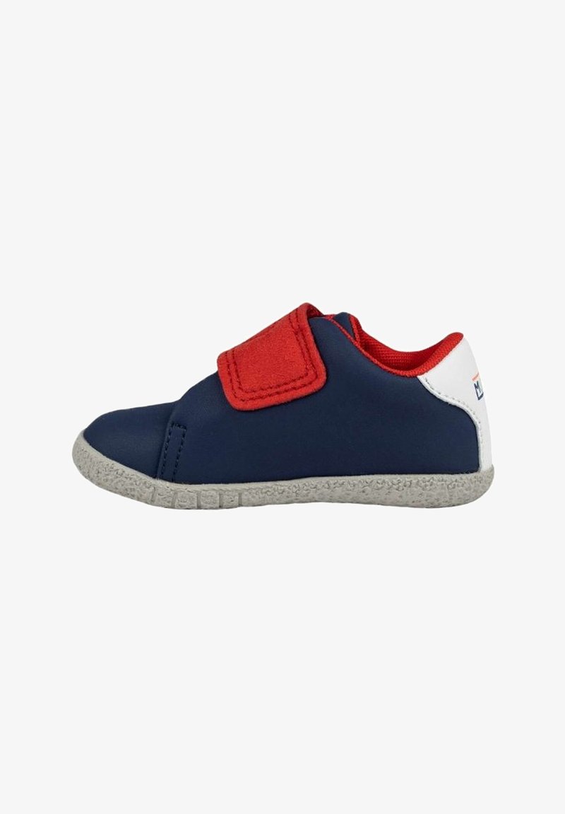 Zapatilla de color azul marino con acentos rojos, una correa de Velcro y suela texturizada gris. Material superior suave con un diseño de corte bajo.