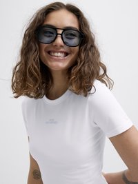 Hvit tettsittende T-skjorte med "CUTE BUT PSYCHO" trykket i lyseblått. Modell som har på seg store svarte solbriller, med bølgete, skulderlangt hår.