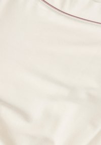 Světlý béžový látka s hladkou texturou, která má jemný lesk a kontrastní úzký vínový lem podél výstřihu.