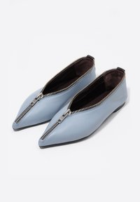 Jasnoniebieskie skórzane buty o ostro zakończonym nosku, z srebrnym zamkiem błyskawicznym wzdłuż górnej krawędzi i ciemną podszewką wewnętrzną.