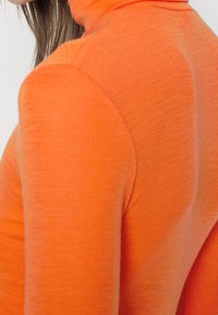 Oranger Rollkragenpullover mit glatter, strukturierter Oberfläche, figurnaher Passform und langen Ärmeln, die eine lebendige, einheitliche Farbe hervorhebt.