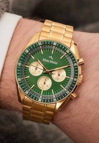 Gouden chronograaf horloge met een groene wijzerplaat, met drie subdials, gouden accenten en een gelinkte metalen band. Het logo "Mats Meier" staat bovenaan.