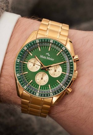 Goldfarbene Chronographuhr mit einem grünen Ziffernblatt, ausgestattet mit drei Teilziffernblättern, goldenen Akzenten und einem verbundenen Metallarmband. Das Logo "Mats Meier" befindet sich oben.