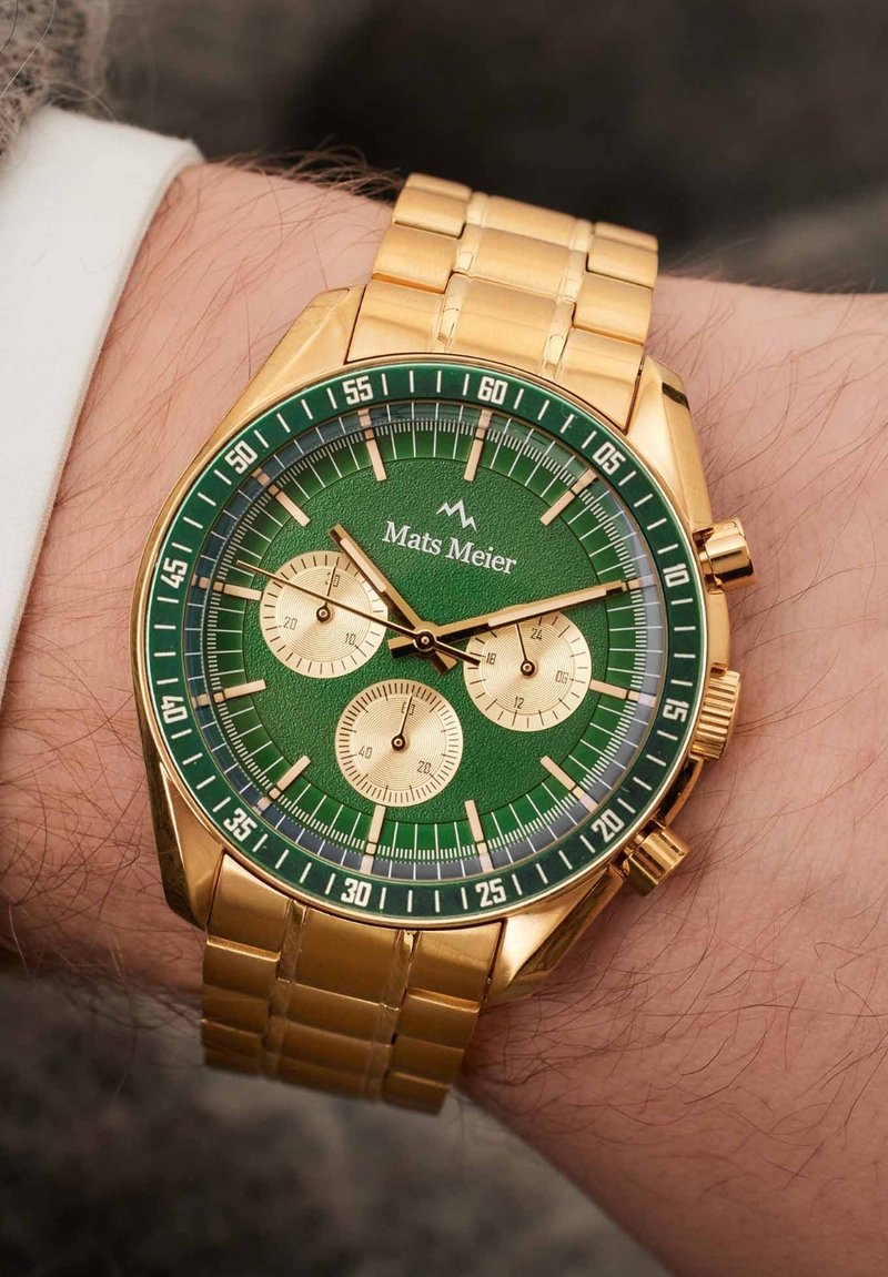Gouden chronograaf horloge met een groene wijzerplaat, met drie subdials, gouden accenten en een gelinkte metalen band. Het logo "Mats Meier" staat bovenaan.