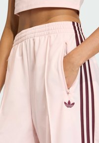 R�óżowe spodnie sportowe o luźnym kroju, wyposażone w dwie boczne kieszenie, elastyczny pas oraz bordowy wzór z trzema paskami, z małym logo.