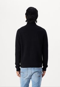 Svart stickad tröja med hög krage, ribbat avslut och långa ärmar. Bärs med ljusblå jeans, som visar fickor med dekorativ sömnad.