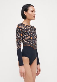 Maillot de bain noir à manches longues avec des motifs floraux en orange et jaune, présentant un design ajusté et des accents texturés le long de l'ourlet.