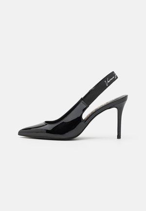 Sort højhælet sko i laklæder med spids tå og slingback, elastikrem med hvid tekst på grå baggrund.