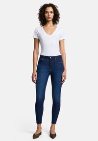 Mörkblå skinny jeans i denim med hög midja, gulddetalj med knapp och sydda fickor, kombinerade med en vit t-shirt med v-ringning.