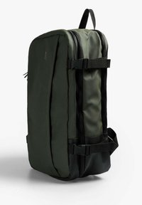 Mochila de color verde oliva con forma rectangular, que cuenta con dos cremalleras, correas ajustables y detalles en negro para un cierre seguro. Tela texturizada.