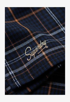 Navy blue check-patterned fabric with orange and light blue lines, detailed with gold embroidered "Superdry" logo. Soft texture, visible weave.