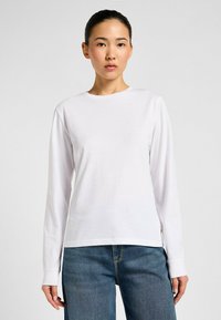 Witte langemouwen shirt van zachte stof met een ronde hals. Gecombineerd met blauwe jeans, die een ontspannen pasvorm en eenvoudig ontwerp tonen.