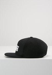 Cappellino da baseball nero realizzato in tessuto, con visiera piatta e un logo ricamato bianco sul davanti. La vista laterale mostra la corona arrotondata.