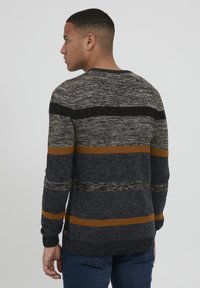Maglione in maglia con strisce grigie, blu navy e nere con dettagli arancioni. Collo rotondo, maniche lunghe, tessuto testurizzato. Senza loghi visibili.