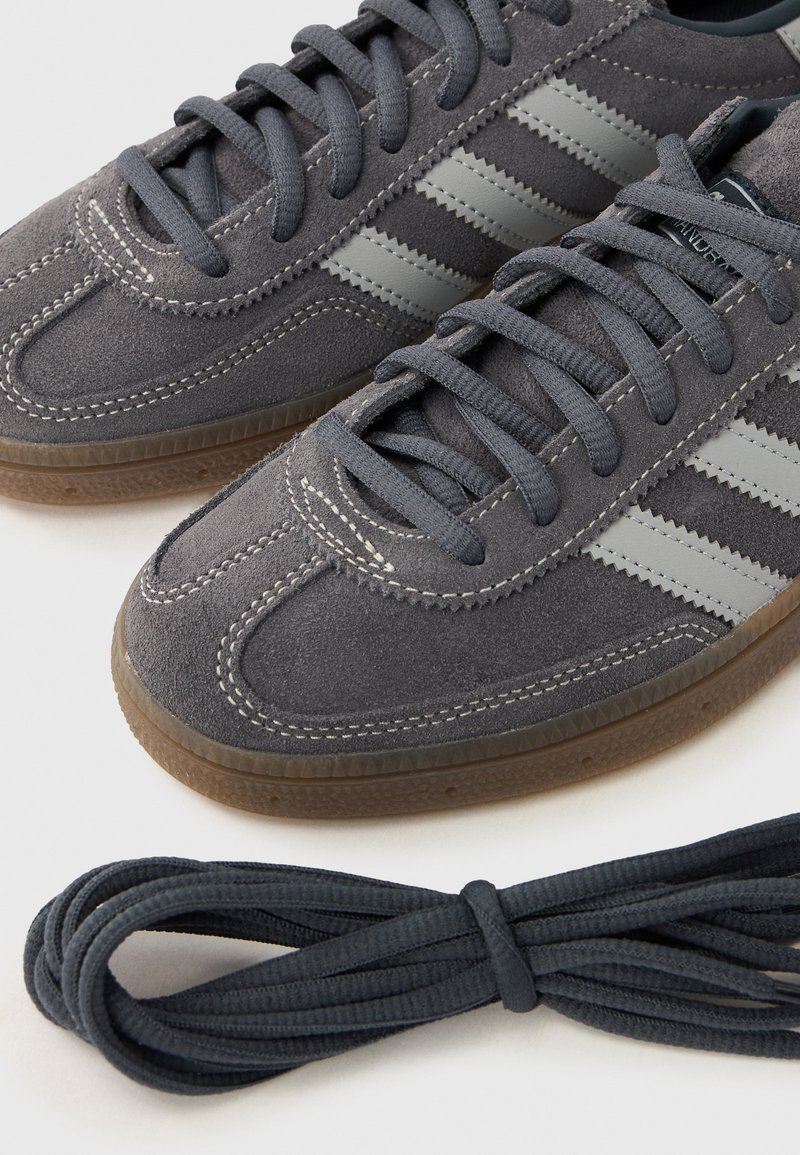 Gray suede sneakers with gray laces, featuring three lighter gray stripes. Includes a coiled matching lace beside the shoes.