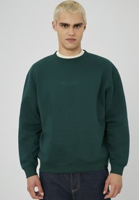 Sweatshirt vert en mélange de coton, avec un col ras du cou, des poignets côtelés et un logo brodé discret à l'avant. Matière lourde, coupe décontractée.