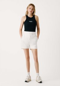 Juoda maikutė su logotipu, balti šortai su raišteliais, pilki sportbačiai ir balti kojinės. Paprastas dizainas, laisvas siluetas, trumpi šortai.