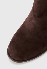 Stivaletto in suede marrone con punta rotonda, texture liscia e design elegante. La suola è di un marrone scuro a contrasto.