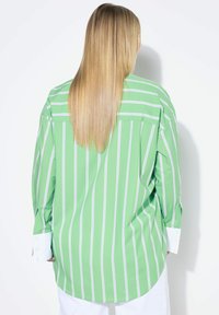 Camicia verde a righe con righe verticali bianche, maniche lunghe con polsini bianchi, vestibilità rilassata e orlo curvo.
