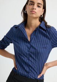 Camicia a maniche corte blu navy con strisce verticali bianche, dotata di colletto classico e realizzata in tessuto leggero e morbido.