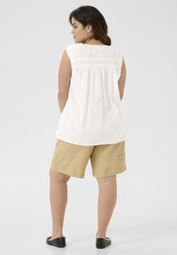 White sleeveless top with gathered detail at back, paired with khaki shorts featuring side pocket, and black flat shoes. Simple, casual outfit.