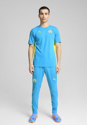 Lichtblauwe sportkleding met gele accenten. Korte mouwen jersey met een gestructureerd patroon en logo. Passende broek en kleurrijke schoenen.