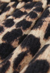 Leopardprintstof med en blød, struktureret overflade i forskellige nuancer af sort og tan, der viser et tydeligt pletmønster.