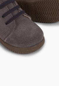 Zapato de ante gris con suela de goma marrón, detalles texturizados y cordones a juego. Punta redondeada con un diseño de bajo perfil.