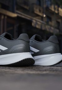 Paire de chaussures de sport grises avec semelles blanches posées sur un pavé extérieur avec un arrière-plan urbain flou.