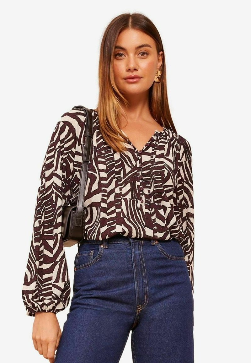 Langärmliges Hemd mit einem schwarz-weißen Zebra-Print, das eine geknöpfte Halslinie und einen lockeren Schnitt aufweist, kombiniert mit hochtaillierten Jeans.