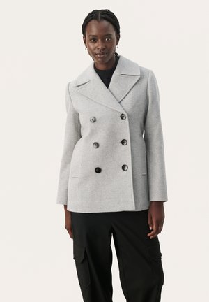 Dubbelzijdige grijze wol coat met grote zwarte knopen, opstaande kraag en zijzakken, gedragen over zwarte broeken. Glad oppervlak.