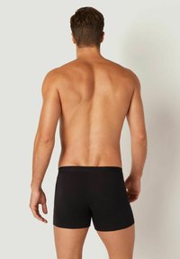 Boxeri negri dintr-un material moale, cu un brâu neted; design ajustat care evidențiază un fundal neutru.