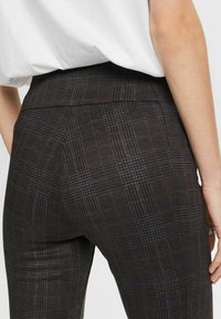 Personne portant un pantalon à carreaux gris foncé et une chemise blanche rentrée, vue de dos à la taille et au-dessus des cuisses.
