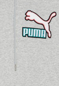 Grå hætte sweatshirt med et stort broderet Puma-logo i hvid og rød samt tyrkis tekst. Materialet har en blød, tekstureret overflade.