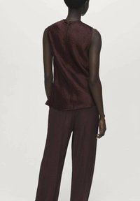 Top senza maniche bordeaux con finitura testurizzata, chiusura a bottone sul retro e vestibilità rilassata, abbinato a pantaloni larghi coordinati.