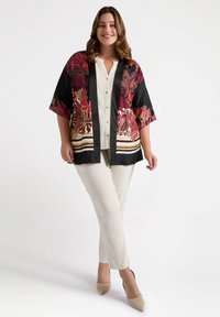 Czarna kurtka w stylu kimono z kwiecistym wzorem w odcieniach czerwieni i beżu, zestawiona z kremową bluzką i jasnobeżowymi spodniami, o miękkiej teksturze i szerokich rękawach.