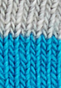 Tessuto lavorato a maglia in grigio chiaro, grigio scuro e turchese; presenta un motivo intrecciato con una consistenza liscia e transizioni di colore ben definite.